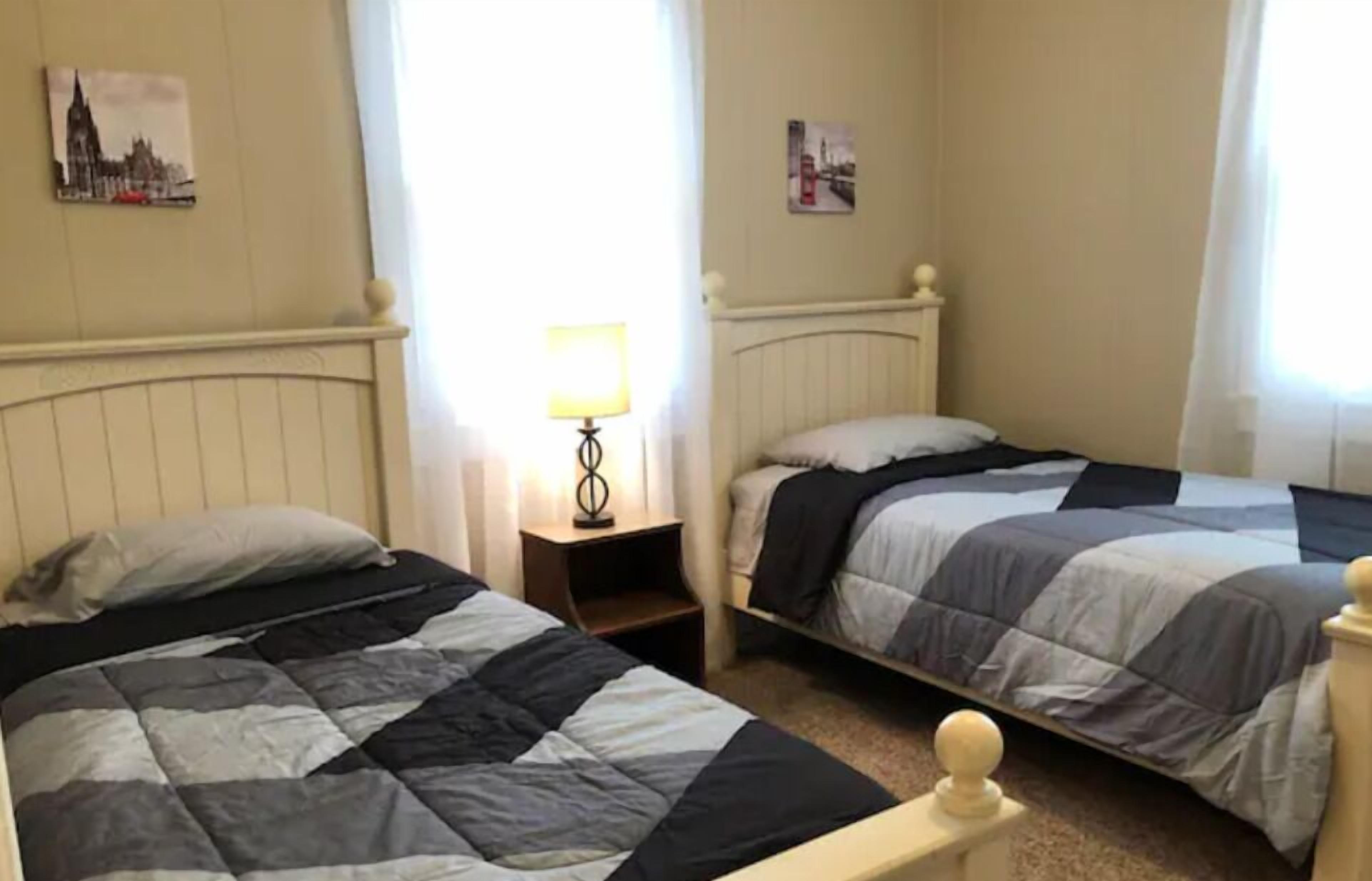 A room with two beds, a nightstand with a lamp, and two wall-mounted pictures.