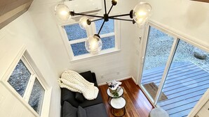 Un interior moderno con una escalera de madera, un sofá negro y un comedor con taburetes.