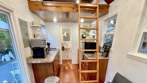 Un espacio habitable compacto con techo de madera, un sofá, otomanas, una zona de comedor y una cocina.