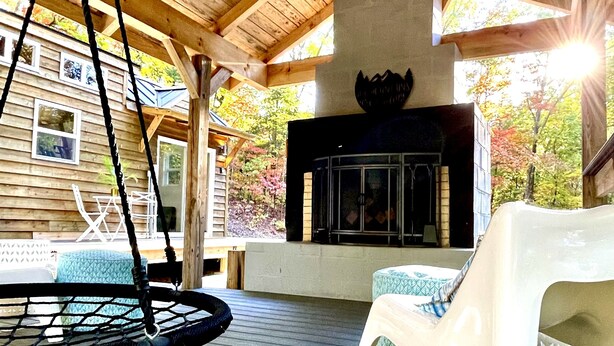 Un espacio al aire libre techado con techo de madera, chimenea y un columpio.