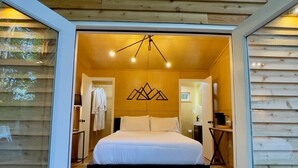 Un dormitorio acogedor con cama, mesita de noche, una silla y un escritorio. Hay una ventana al lado izquierdo de la habitación.