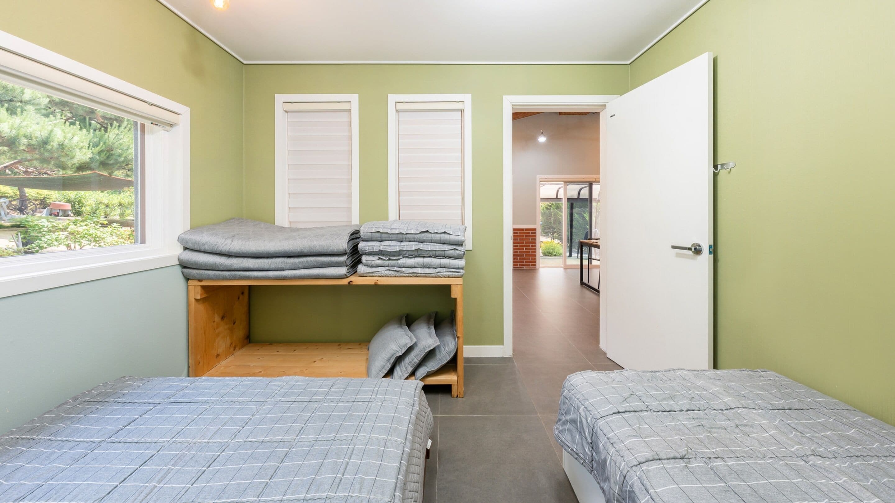 Una habitación pequeña y luminosa con dos camas, una ventana y una puerta que da a otra habitación.