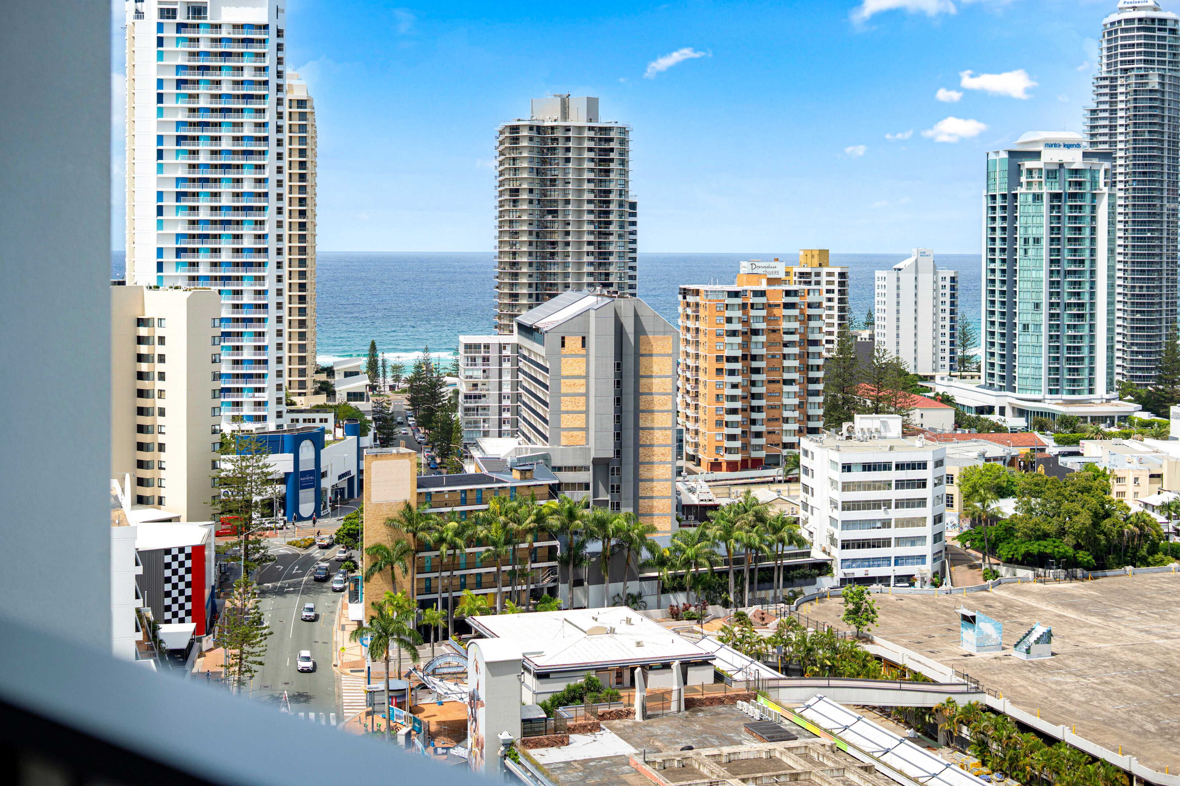 A cityscape with high-rise buildings, a road, and palm trees.