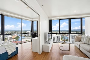 Un apartament modern amb grans finestres, un llit, escriptori, televisor i sofà.