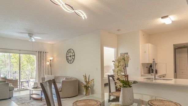 Un salon moderne avec une table à manger en verre, des canapés beige et une grande fenêtre.