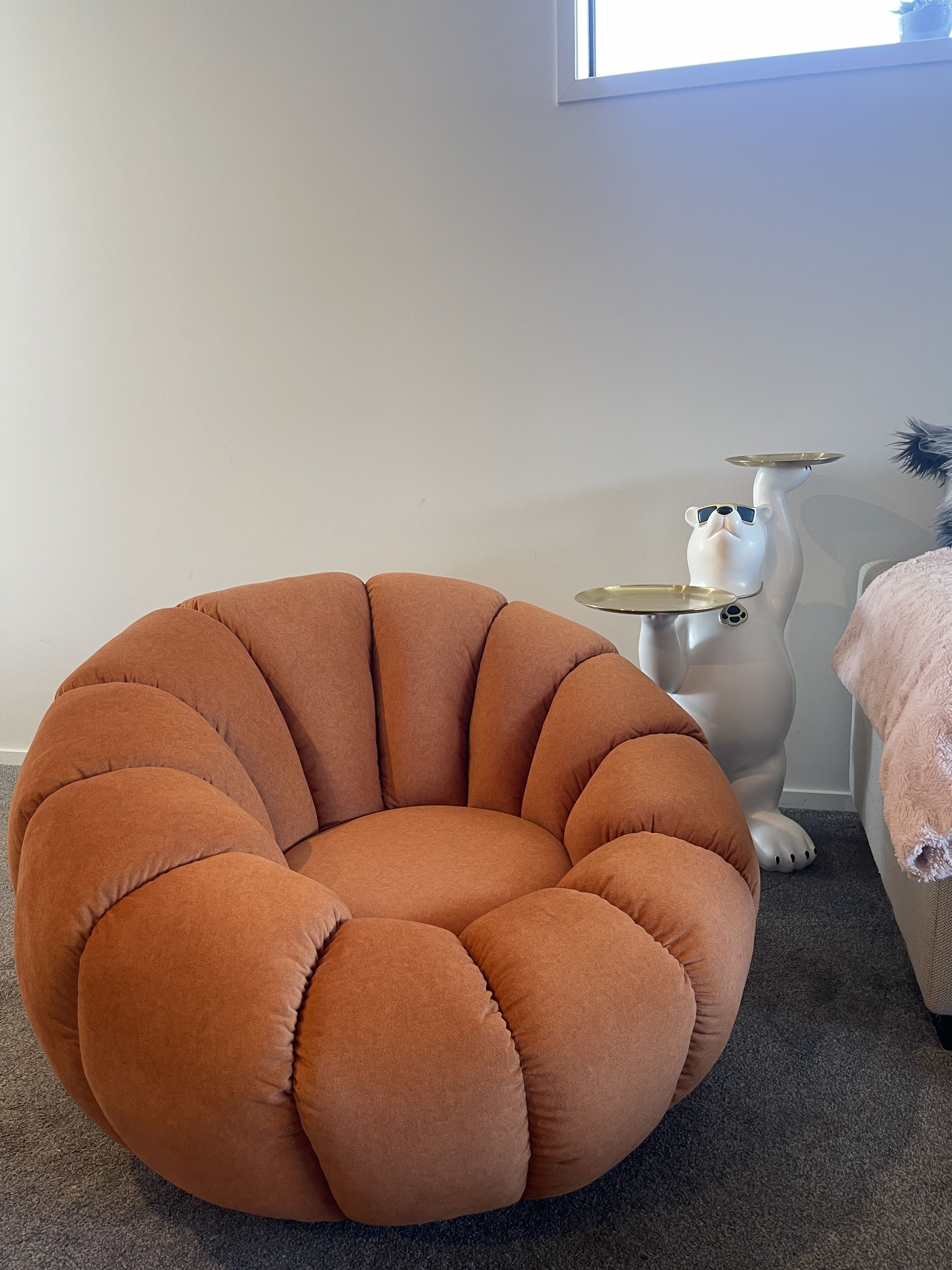 A round, orange armchair with a high backrest and a side table with a white ceramic cat statue.