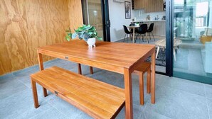 Un comedor moderno con una mesa y banco de madera, una planta en maceta y vistas a una cocina y comedor a través de una puerta de cristal.