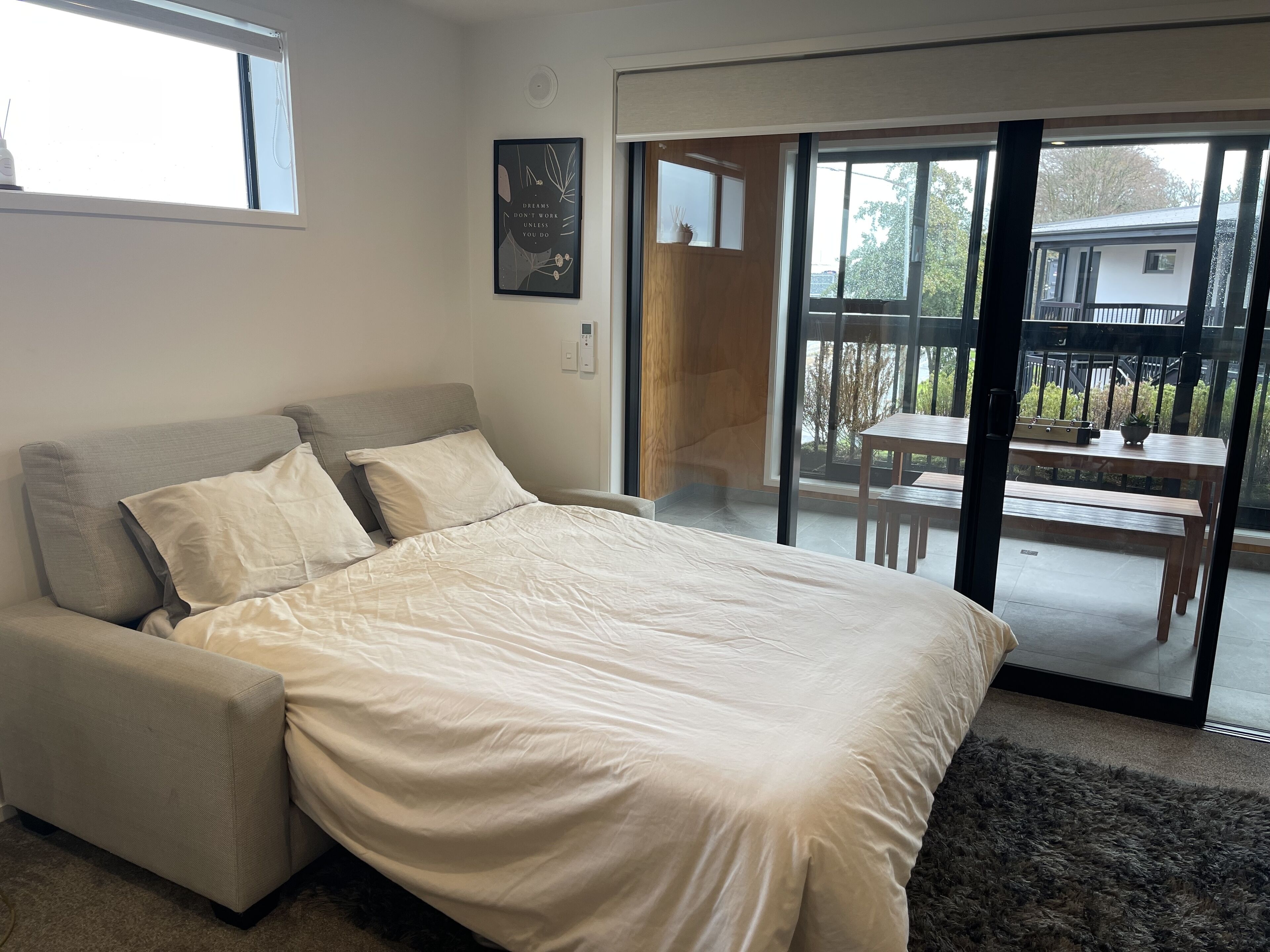 Un dormitorio con cama, sofá, puerta corrediza de cristal a un balcón y una cita enmarcada en la pared.