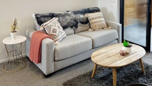 Una sala de estar moderna con un sofá gris, una mesa de centro redonda de madera y un ventanal grande.