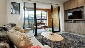 Una sala moderna con un sofá, una mesa de centro y un televisor en el área de la cocina contigua.