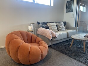 Ett vardagsrum med en grå soffa, en rund, orange fåtölj, ett litet runt soffbord och en mjuk, grå matta.