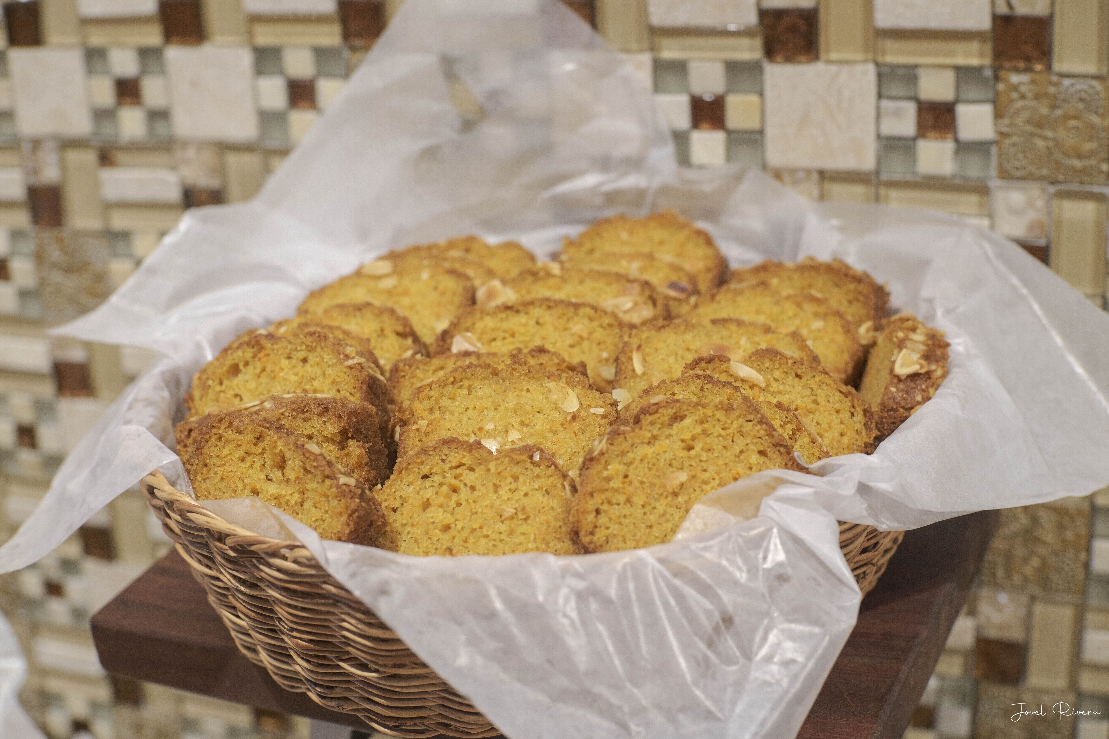A basket of cookies on a wooden table with a tiled backsplash in the background.