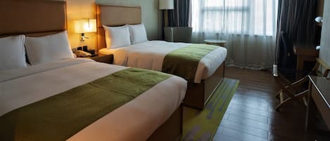 A hotel room with two beds, a desk, a chair, and a window with curtains.