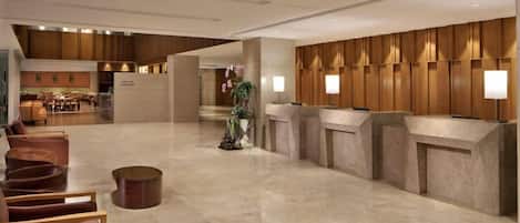A spacious lobby with a reception desk, seating area, and a view into a restaurant.