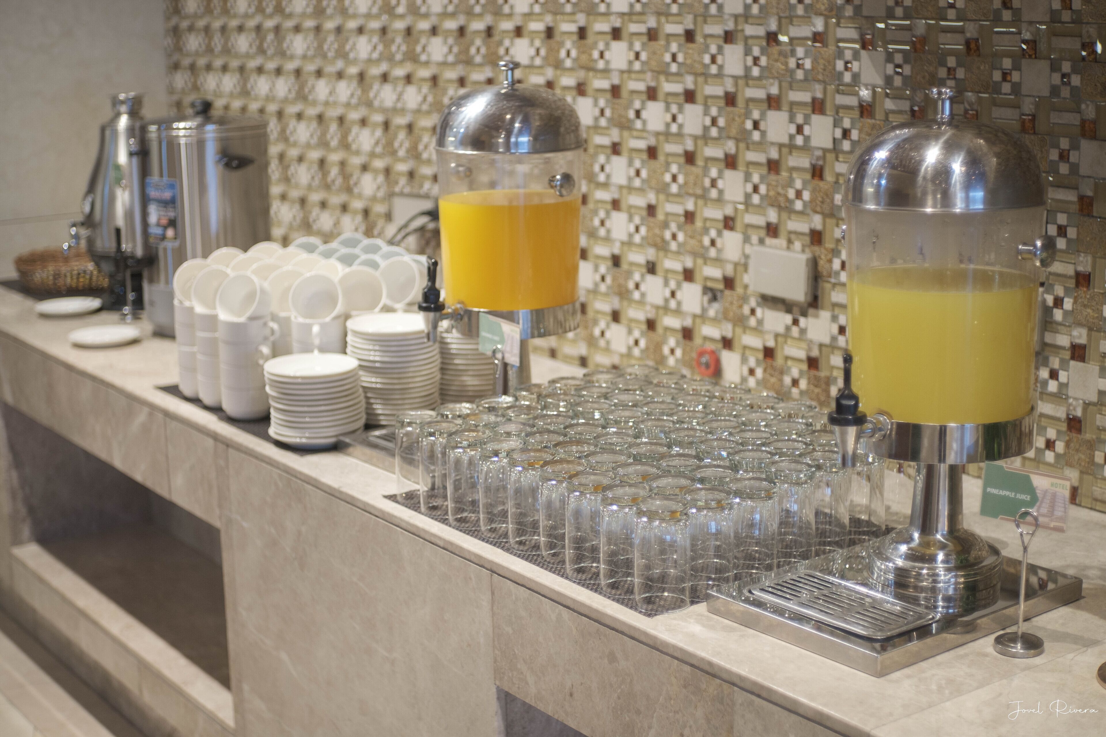 A buffet setup with multiple juice dispensers, stacked plates, and glasses.