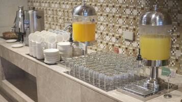 A buffet setup with multiple juice dispensers, stacked plates, and glasses.