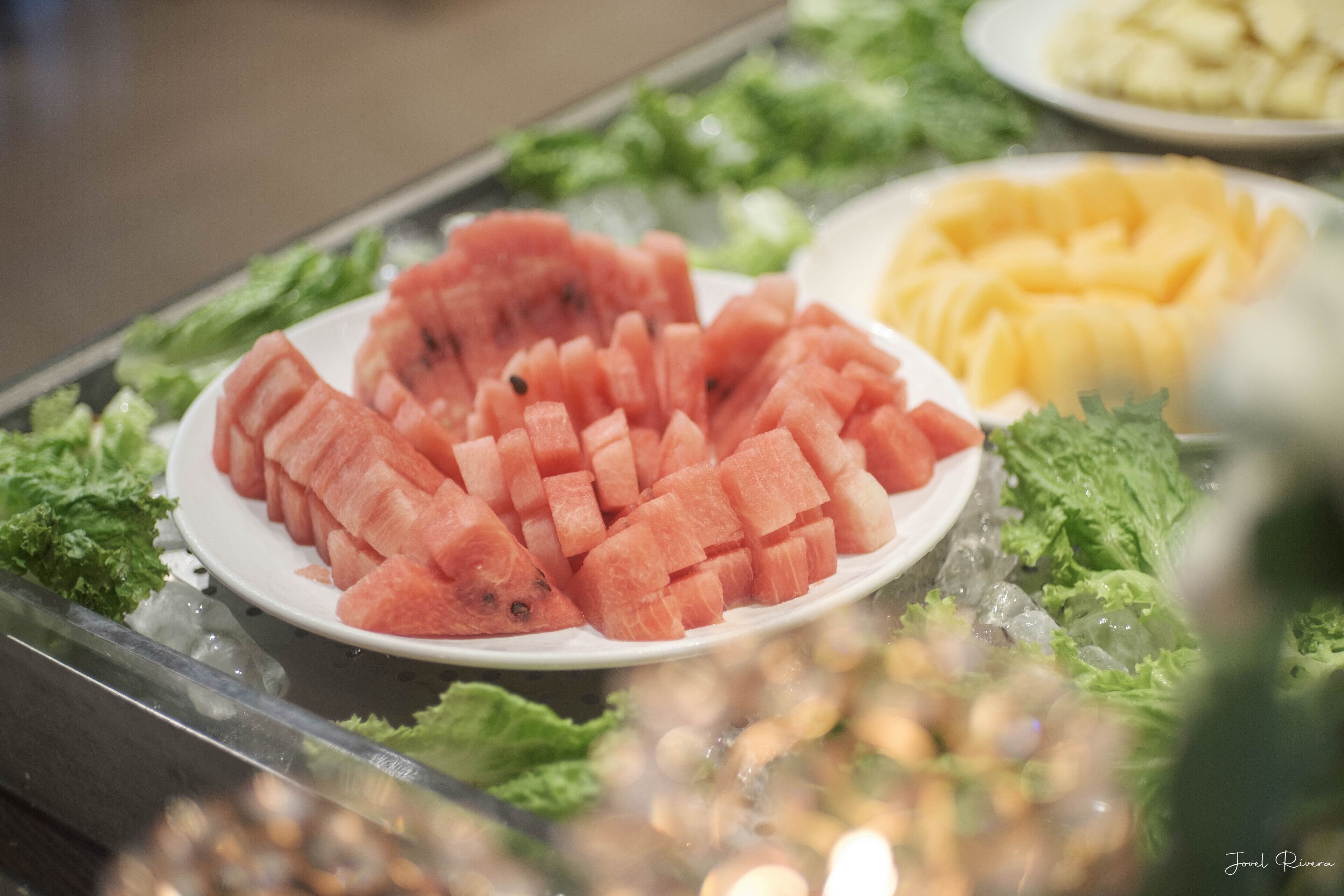 En tallrik med tärnad vattenmelon och en tallrik med skivad mango, serverat på ett bädd av sallad.