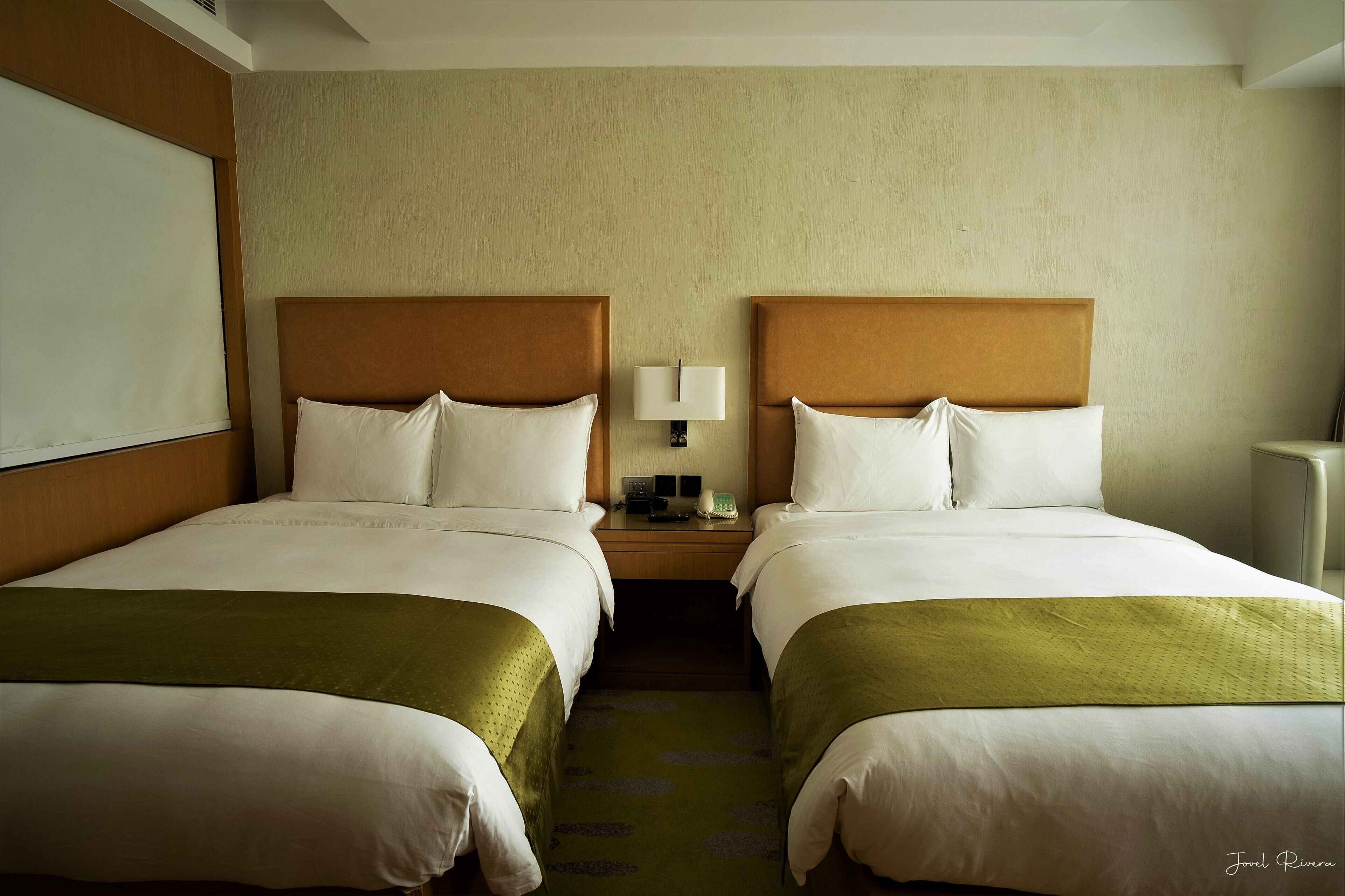 Ein Hotelzimmer mit zwei Betten, einem Nachttisch mit Lampe und einem großen Fenster.