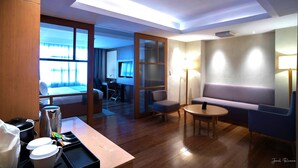 A hotel room with a wooden floor, a sofa, a small table, a coffee machine, and a bed with a view of the outdoors. - Ion Hotel (Baguio)