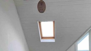 Un dormitorio acogedor en el ático con techo inclinado, un tragaluz, una cama con un cojín que dice 'hello sunshine', una mesita auxiliar pequeña y una alfombra redonda.