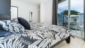A bedroom with a large bed, a ceiling fan, a window with a view of buildings, and a balcony. - *NEW* Casita Lalita -  2bd/2.5 ba condo - 5 mins to beach w/ 200mbps wifi + pool (Tamarindo)