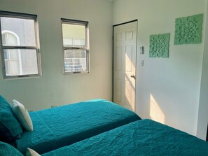 Un dormitorio con dos camas, dos ventanas, una puerta y decoración en la pared.