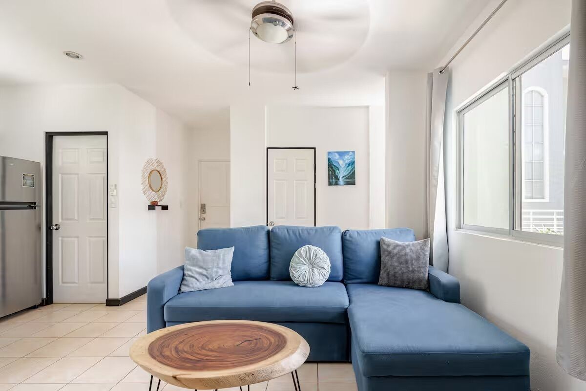 Un salon moderne avec un canapé d’angle bleu, une table basse en bois et une grande fenêtre laissant entrer la lumière naturelle.