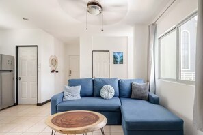 Un salon moderne avec un canapé d’angle bleu, une table basse en bois et une grande fenêtre laissant entrer la lumière naturelle.