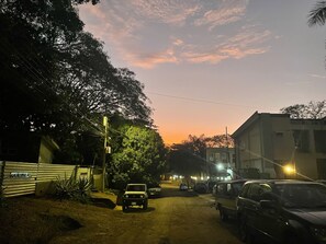 A street at dusk with parked cars, a building with a sign reading "CASA DEBEACH", and trees lining the road. - *NEW* Casita Lalita -  2bd/2.5 ba condo - 5 mins to beach w/ 200mbps wifi + pool (Tamarindo)