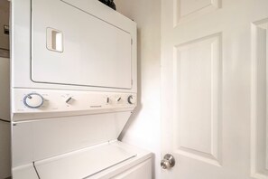 Un appareil combiné lave-linge et sèche-linge blanc, de type à chargement vertical, doté de boutons de commande et d’une porte.