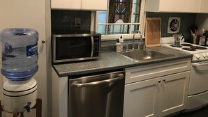 Una cucina con mobili bianchi, un forno a microonde in acciaio inossidabile, un lavello e un dispenser per l'acqua.