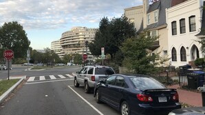 Una vista di strada con un segnale di stop, un attraversamento pedonale e auto parcheggiate.