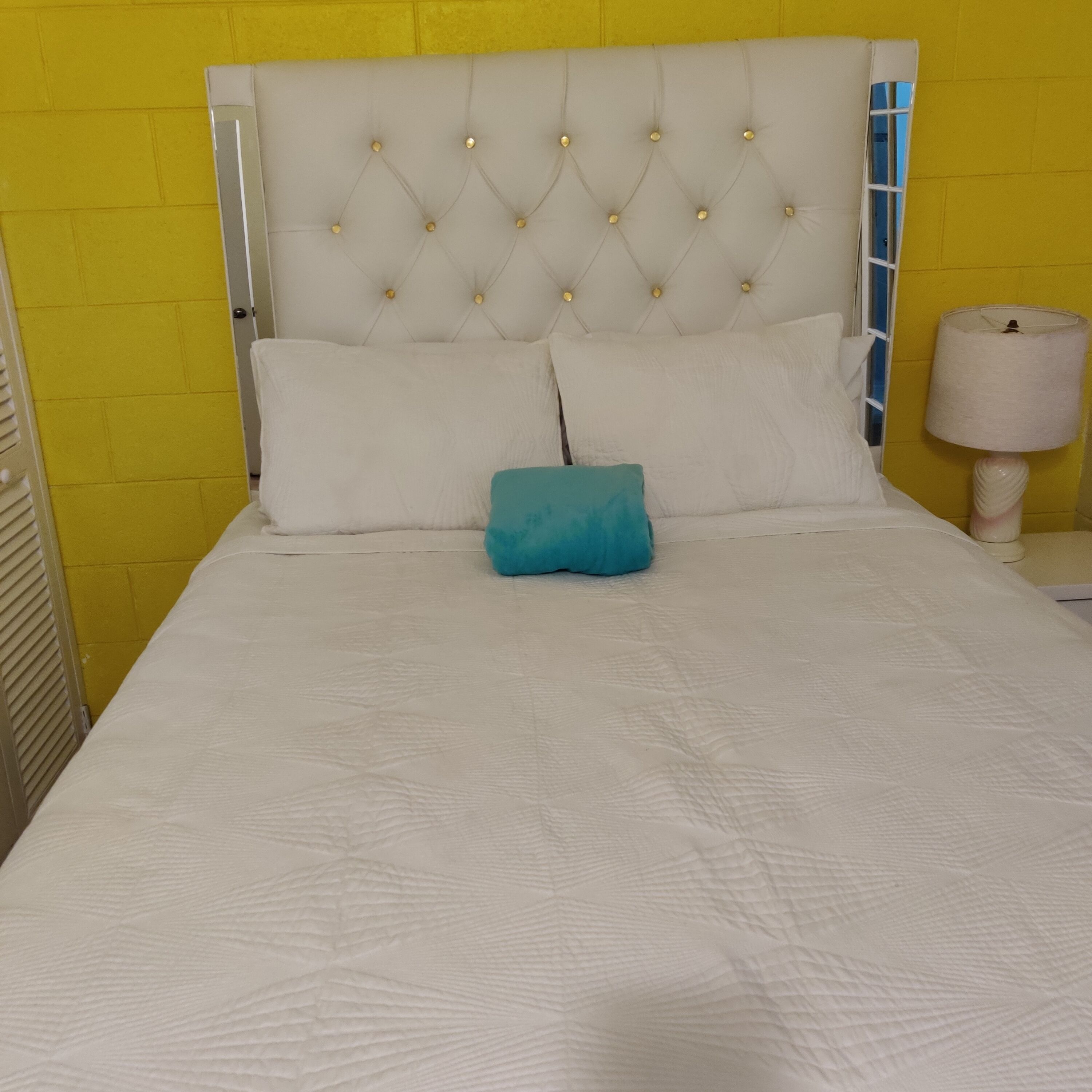 A bed with a tufted headboard, two pillows, and a blue accent pillow.