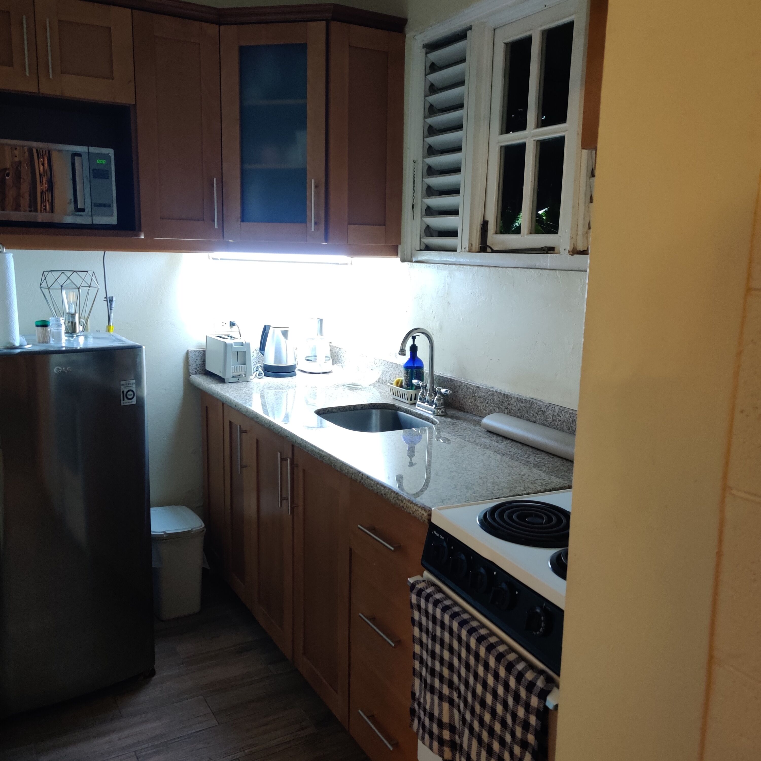A kitchen with wooden cabinets, a stainless steel refrigerator, a sink, a stove, and a window with blinds.