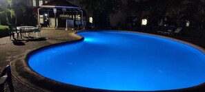 A swimming pool with a curved edge, surrounded by lounge chairs and a covered seating area.