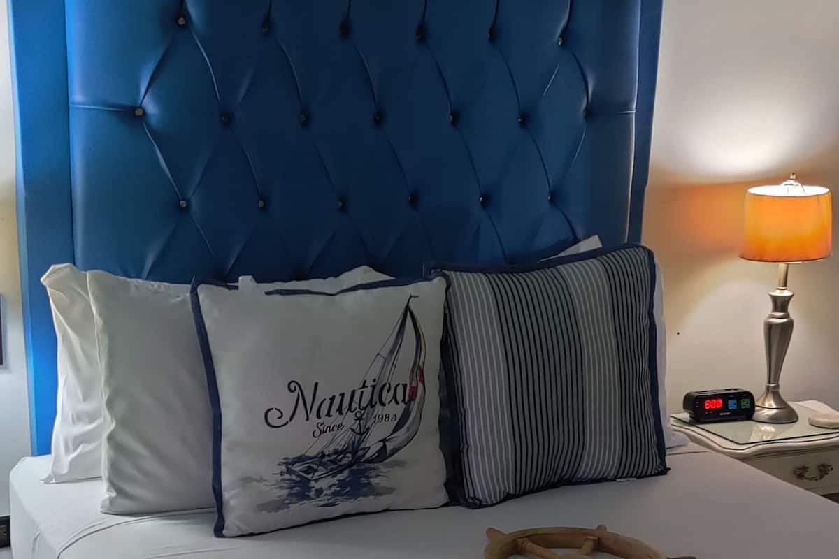 A bed with a blue headboard, white bedding, and a wooden ship wheel decoration.