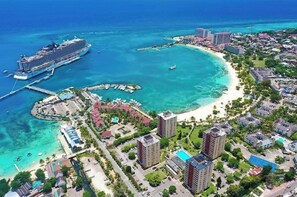 A coastal resort with a large cruise ship docked, a sandy beach, and a marina.