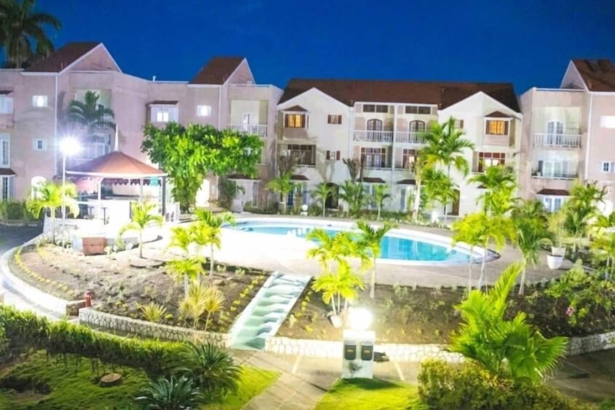 A hotel with a swimming pool surrounded by palm trees and a waterfall feature.