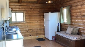 Una cocina compacta con paredes de madera, un refrigerador, una estufa y un lavabo.
