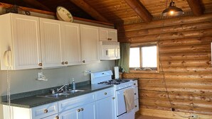 Una cocina con vigas de madera, armarios blancos, una estufa y un microondas.