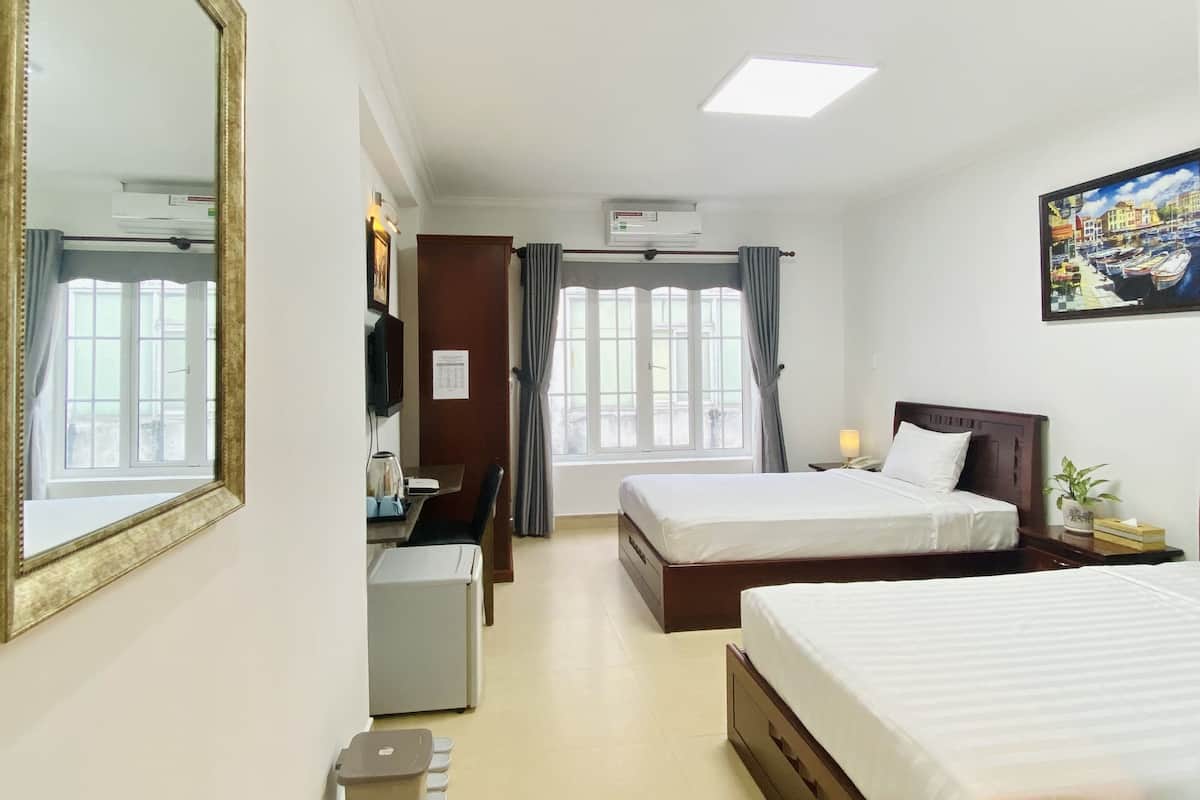 Ein Hotelzimmer mit zwei Betten, einem Schreibtisch, einem Stuhl, einem Fernseher und einem Bild an der Wand.