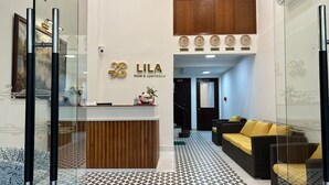 A hotel reception area with a wooden reception desk, a wall-mounted clock displaying multiple time zones, and a seating area with a patterned floor. - LILA Hotel & Apartments (Ho Chi Minh City)
