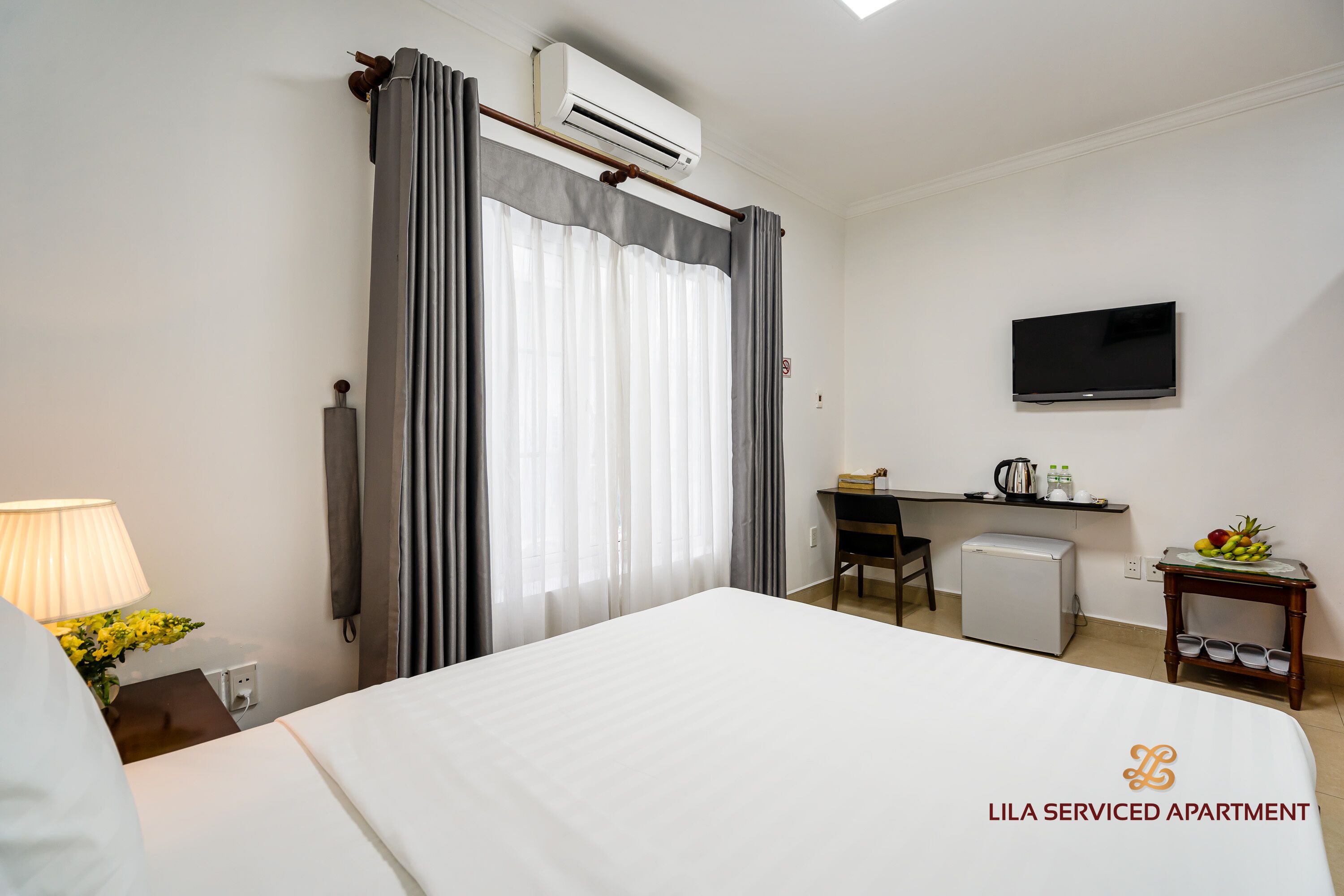 A bedroom with a bed, a desk, a chair, a TV, and a small refrigerator.