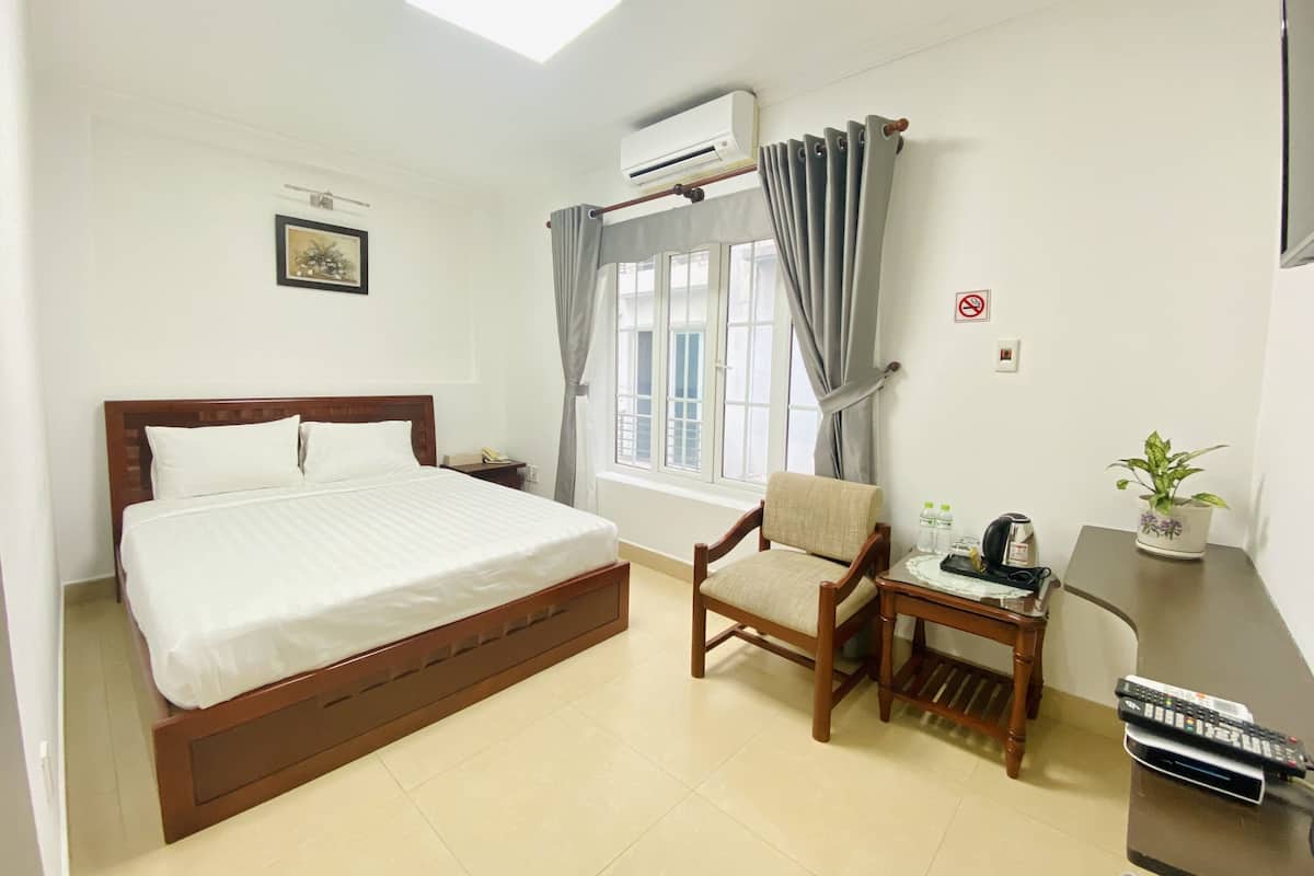 Ein Hotelzimmer mit Bett, Stuhl, kleinem Tisch mit Pflanze, Fernbedienung und einem Rauchverbot-Schild.