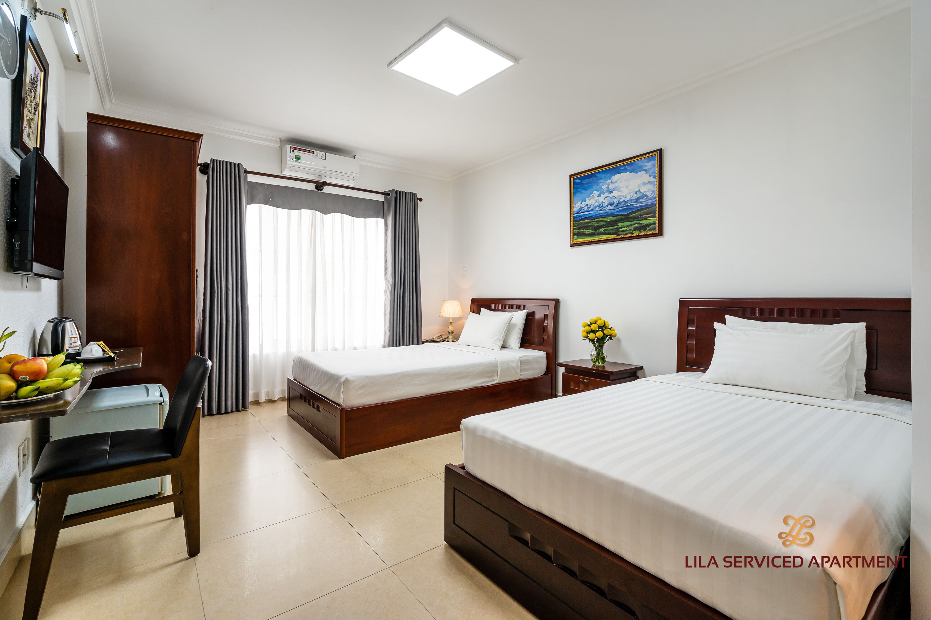 A hotel room with two beds, a desk with a chair, a TV, and a window with curtains.