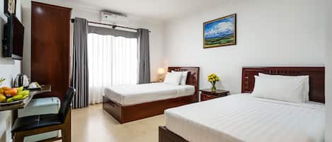 A hotel room with two beds, a desk with a chair, a TV, and a window with curtains.