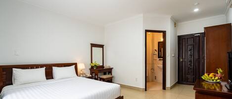 A hotel room with a large bed, a bedside table with a lamp, a mirror, a wooden wardrobe, and a bathroom visible through an open door.