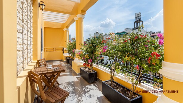 A yellow balcony with wooden furniture and potted plants. - LILA Hotel & Apartments (Ho Chi Minh City)