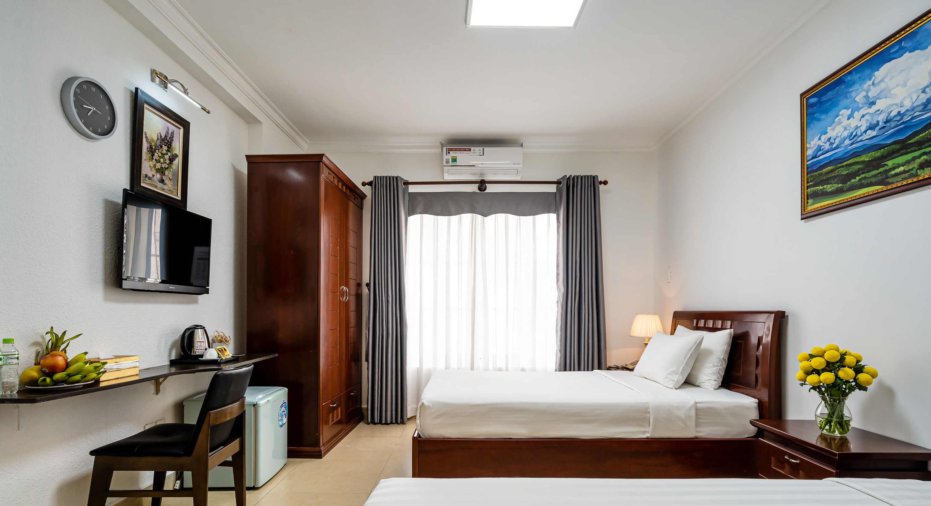 A hotel room with a bed, a desk with a chair, a television, a clock, and a painting.