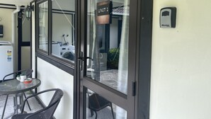 A room with a glass door, a small table with chairs, a washing machine, and a Master Lock on the wall. - Westminster Mount View Unit 1 (Rotorua)
